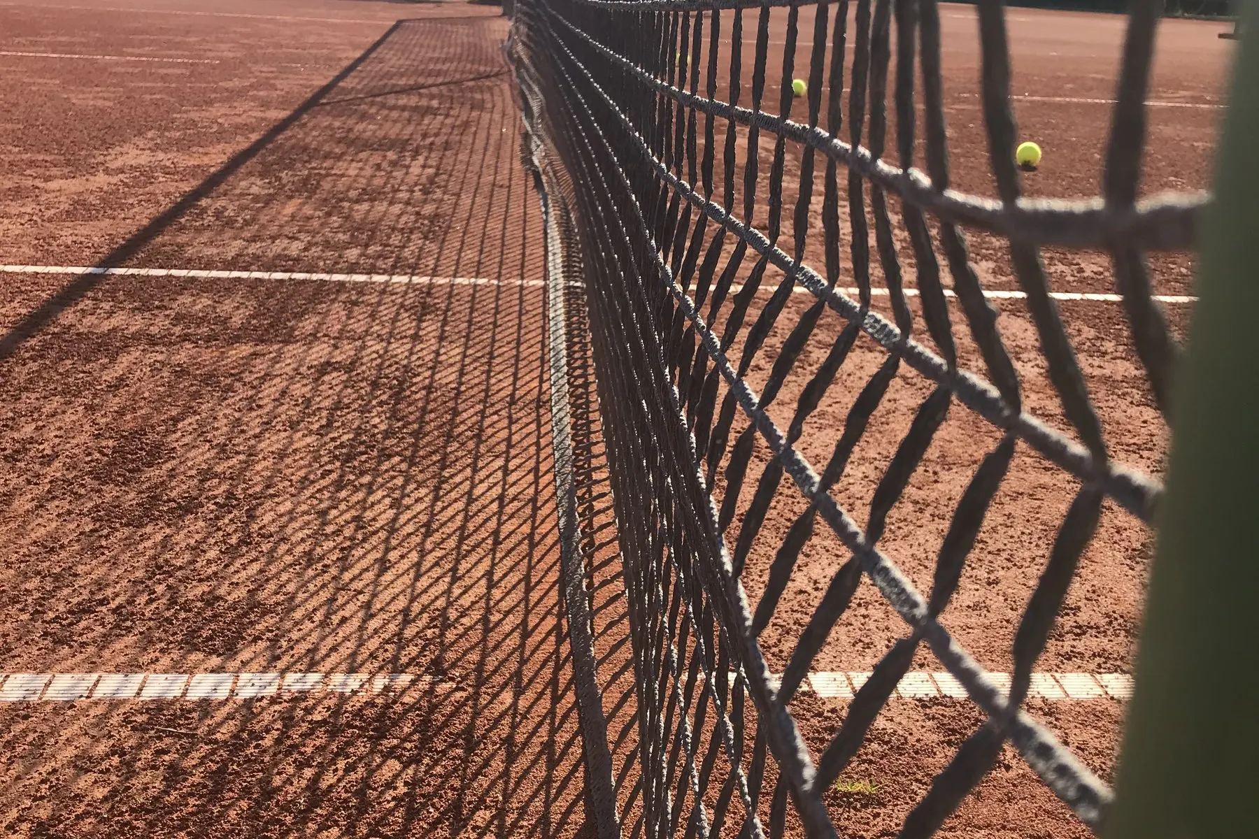 Blick entlang des Tennisnetzes über den Sandplatz