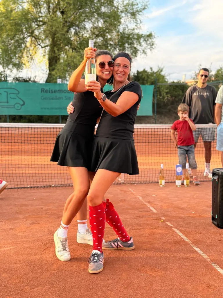 Zwei Spielerinnen jubeln mit einer Flasche Wein auf dem Platz